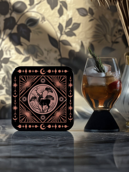 A set of four black, high-gloss square coasters featuring intricate rose-gold metallic illustrations of an owl, raven, stag, and wolf framed by celestial and botanical motifs. Made from durable masonite hardboard with cork backing for slip-resistant protection.